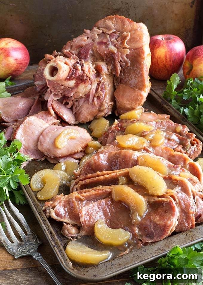 Sliced Apple Pie Ham on a baking sheet next to fresh herb bunches