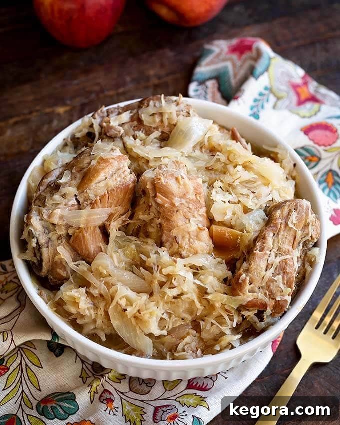A close-up shot of slow-cooked pork and sauerkraut nestled in a white bowl, garnished with fresh herbs, resting on a charming floral napkin beside a gold fork.