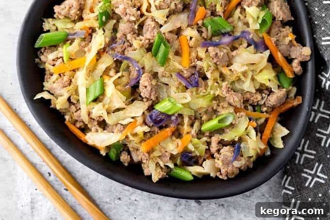 A black bowl filled with Instant Pot Egg Roll in a Bowl, garnished generously with vibrant green onions, positioned next to a pair of bamboo chopsticks.