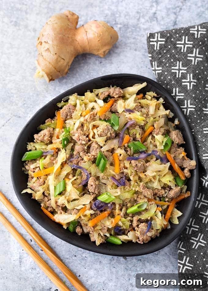 Instant Pot Egg Roll in a Bowl presented in a black bowl, flanked by wooden chopsticks and fresh ginger root, highlighting the wholesome ingredients and the enticing finished dish.