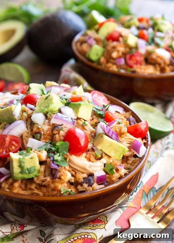 Two Chicken Taco Bowls in brown bowls topped with diced red onion, avocado, and cherry tomatoes, showcasing a fresh and vibrant meal.