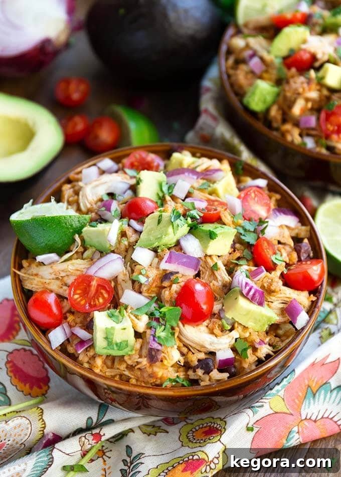 Two Chicken Taco Bowls in brown bowls topped with diced red onion, avocado, and cherry tomatoes, ready for serving or meal prep.