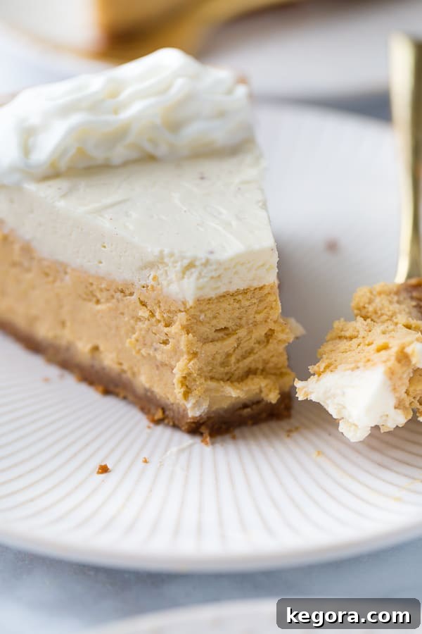 Decadent Gluten-Free Pumpkin Cheesecake 9 A close-up shot of a slice of gluten-free pumpkin cheesecake on a white plate with a fork, ready to be eaten.