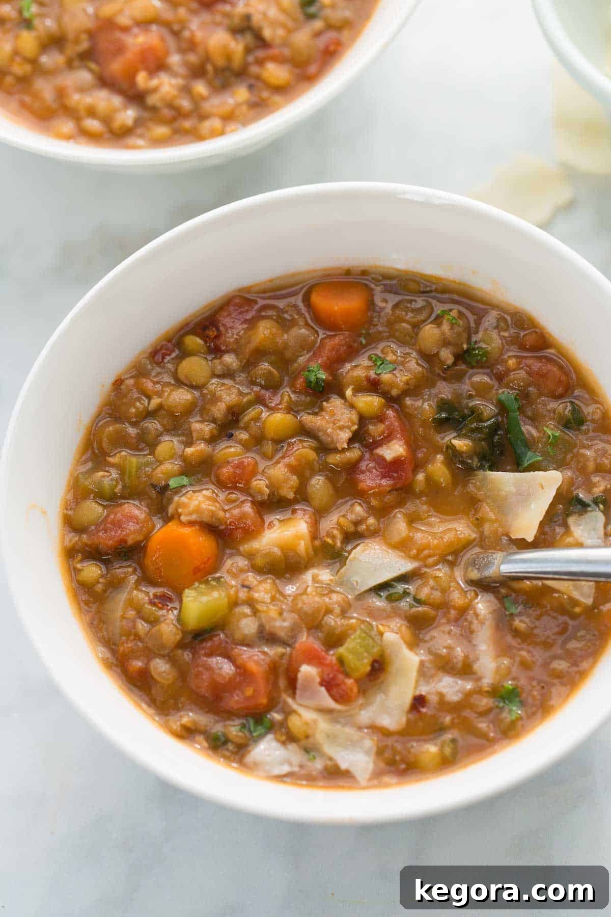 Hearty Sausage Lentil Soup 4 Üzerine taze Parmesan peyniri ve otlarla süslenmiş, doyurucu bir kasede sosisli mercimek çorbası.