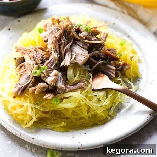 Flavorful berry maple pulled pork served over spaghetti squash on a white plate with black speckles, accompanied by a fork.