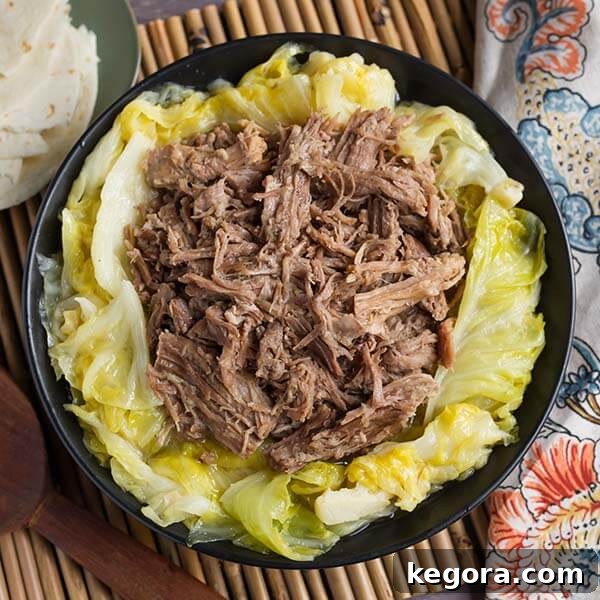 Succulent Instant Pot Kalua Pork served over tender cooked cabbage in a black bowl, a simple yet intensely flavorful dish.