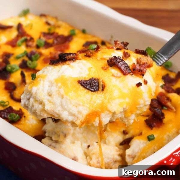 A creamy, cheesy baked cauliflower casserole in a white and red baking dish, with a serving spoon scooping out a generous slice.