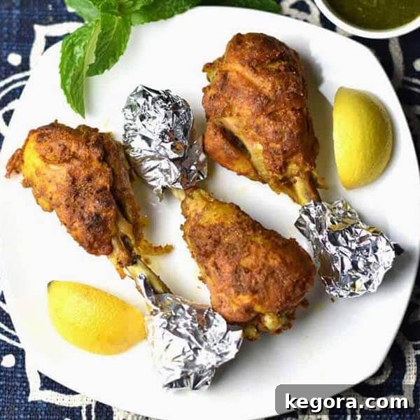 Tandoori Chicken drumsticks beautifully arranged on a white plate with lemon wedges, featuring foil-wrapped bones for easy handling.