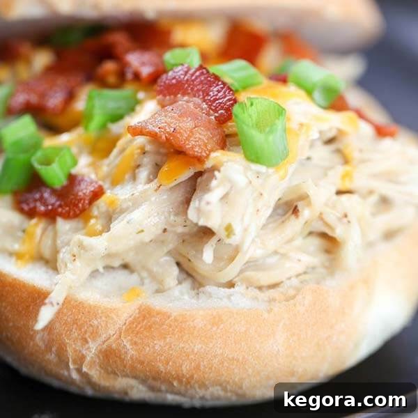 A close-up shot of creamy Instant Pot Crack Chicken, richly flavored with ranch, smoky bacon, and melted cheese, served on a hamburger bun.