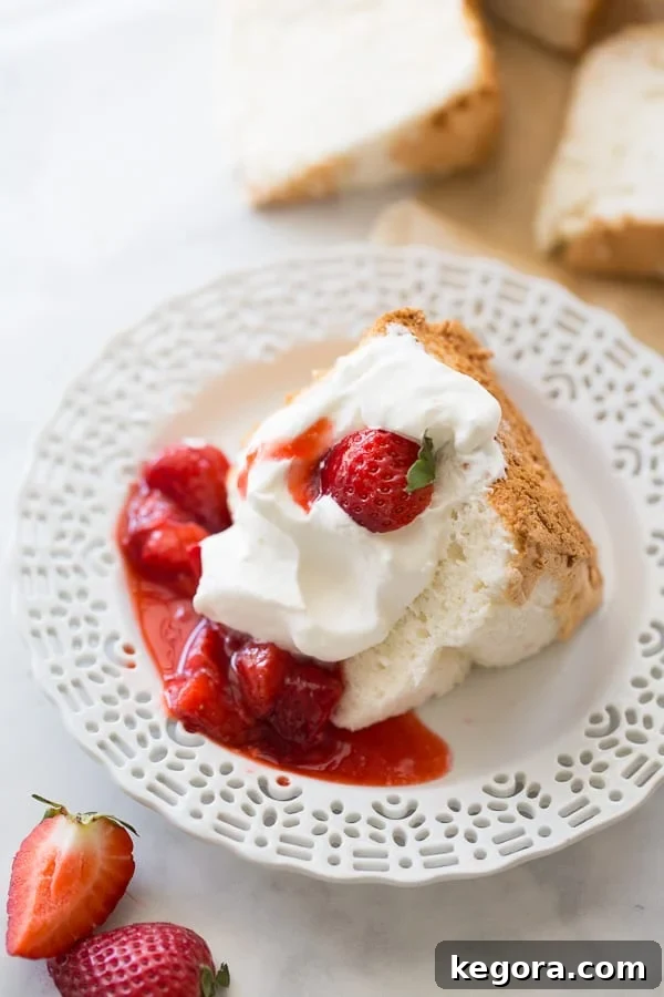 A beautiful slice of light and fluffy gluten-free angel food cake, perfectly golden, served on a white plate with fresh, vibrant strawberries on the side. This image showcases the delicate texture and inviting presentation of a classic homemade dessert.