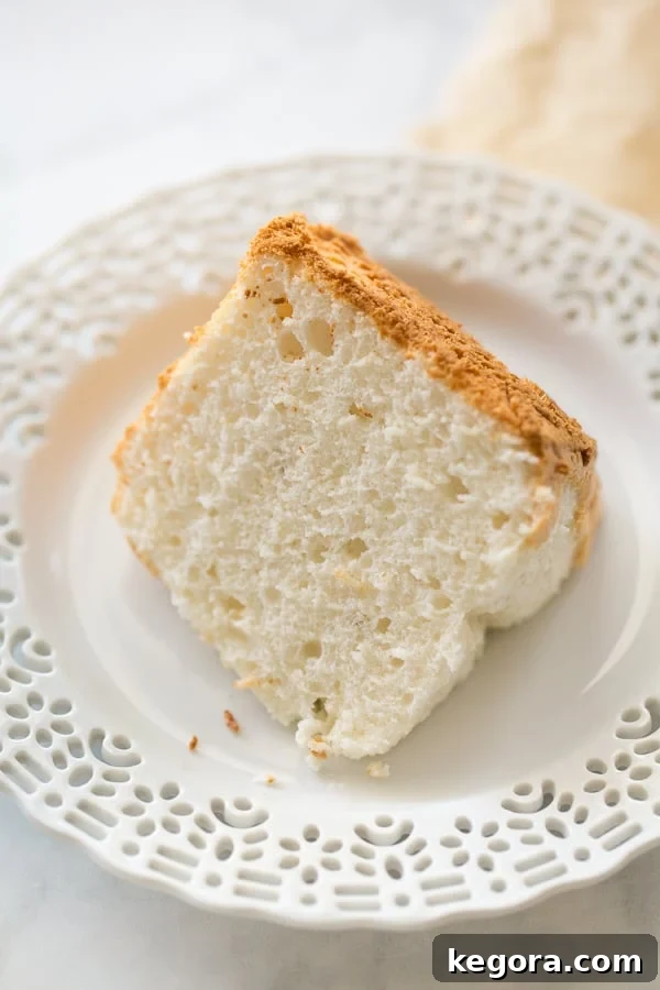 A pristine slice of homemade gluten-free angel food cake resting on a white plate, highlighting its airy crumb and delicate texture. A perfect foundation for any topping.