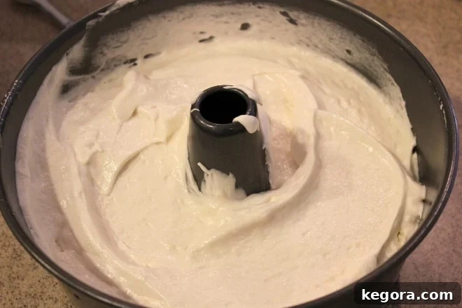 Gluten-free angel food cake batter evenly spread in an ungreased tube pan, ready for baking to achieve its signature height and light texture.