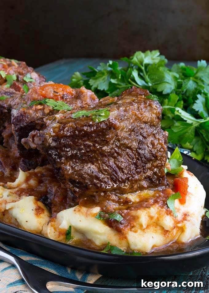 Tender Instant Pot Short Ribs 2 instant pot Short Ribs over mashed potatoes on a black plate next to a bunch of fresh parsley