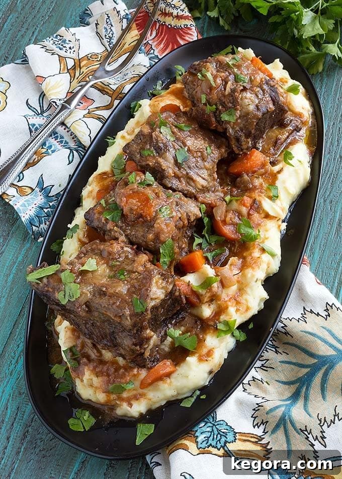 Tender Instant Pot Short Ribs 3 Top view of Short Ribs over mashed potatoes on an oblong black plate
