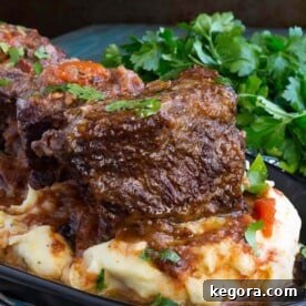 Tender Instant Pot Short Ribs 5 Short Ribs over mashed potatoes on a black plate next to a bunch of fresh parsley
