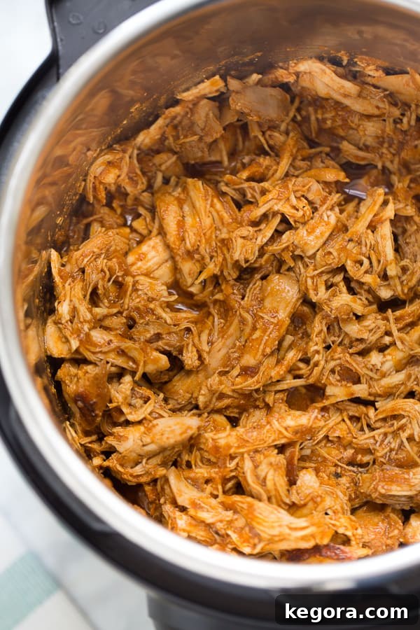 Close-up shot of juicy, shredded Instant Pot BBQ chicken in a pressure cooker with fresh herbs