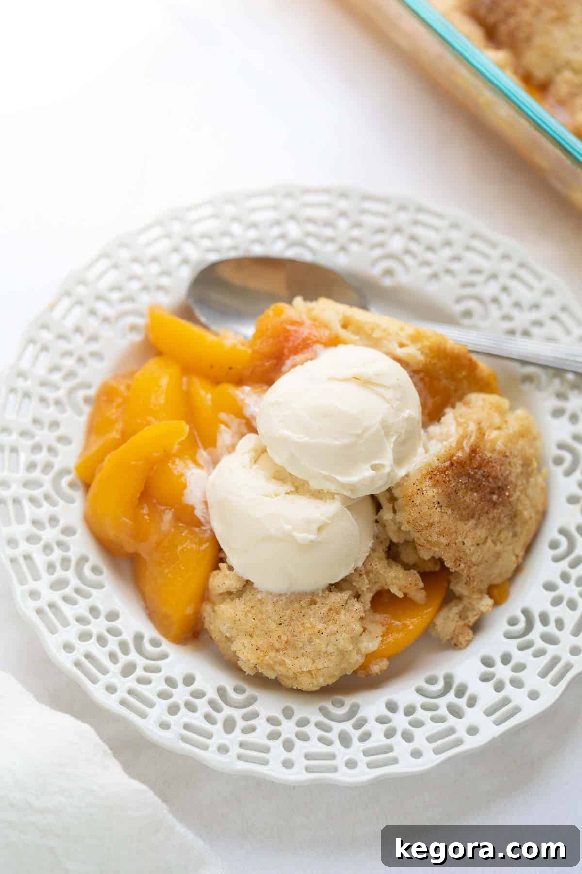 Decadent gluten-free peach cobbler topped with vanilla ice cream, served in a white dish, showcasing its golden crust and juicy filling.