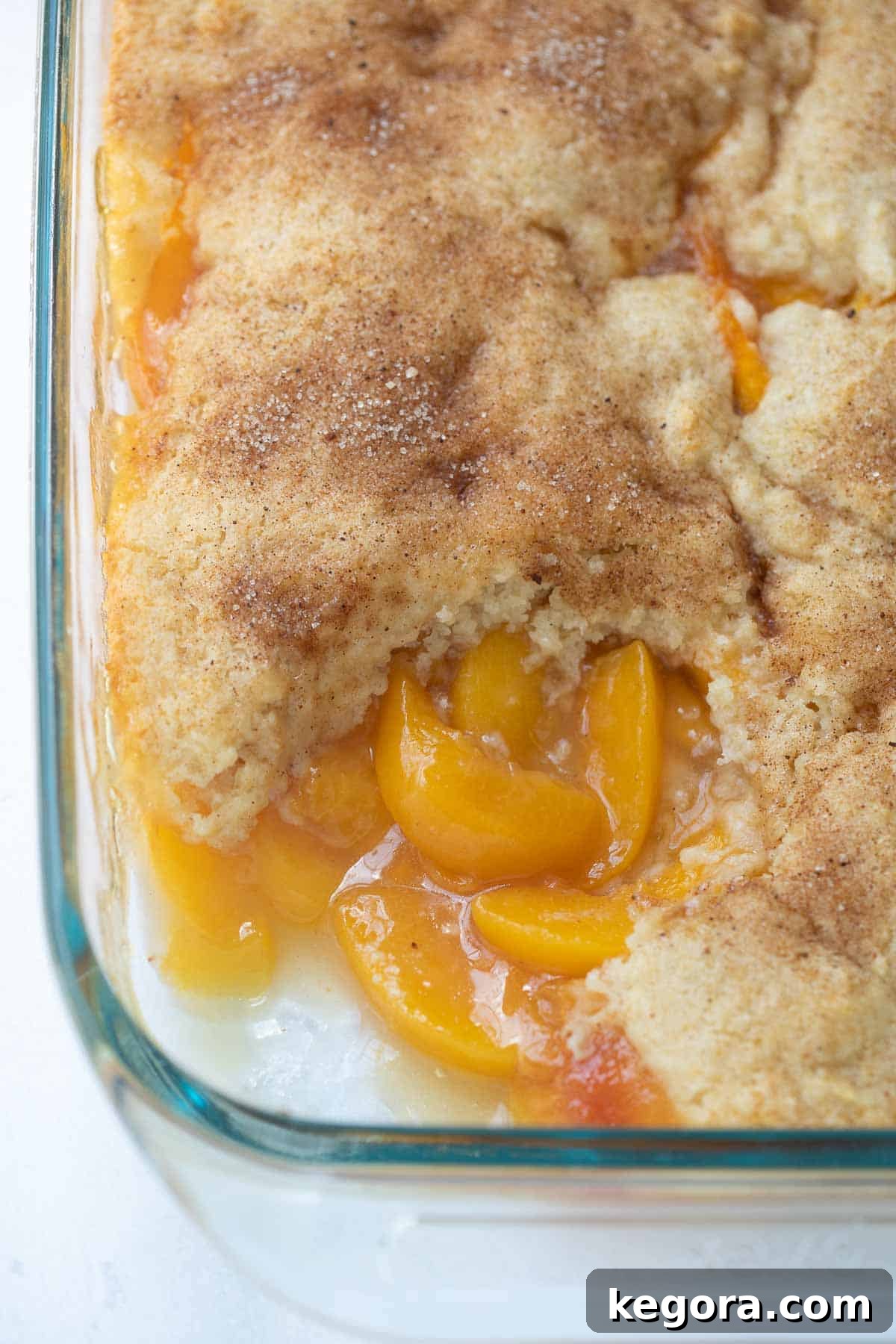 Close-up shot of a baked gluten-free peach cobbler in a pan, highlighting its golden, bubbly fruit filling and soft, inviting topping.
