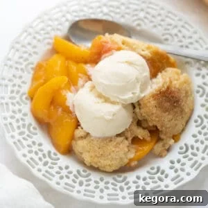 Gluten-free peach cobbler on a white plate, showcasing a slice with golden topping and juicy peaches.
