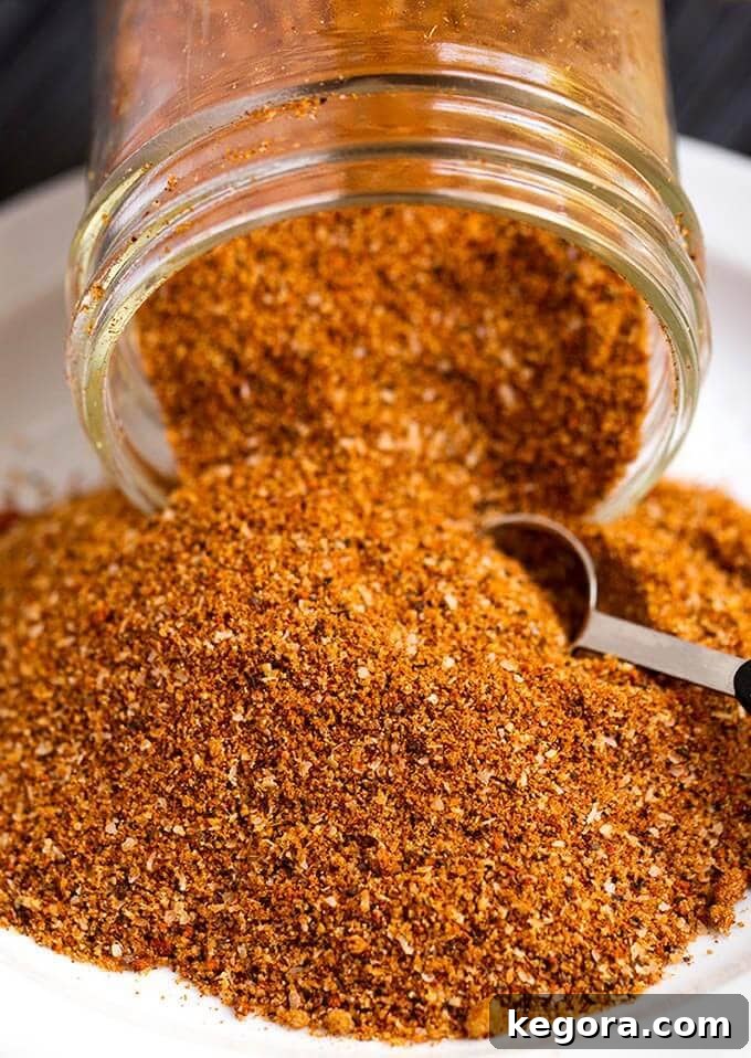 Ultimate Rib Rub 2 Ribs Spice Rub spilling out of a small glass jar with a measuring spoon scooping spice
