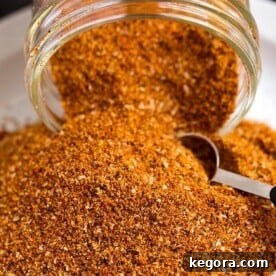 Ultimate Rib Rub 4 Ribs Spice Rub spilling out of a small glass jar with a measuring spoon scooping spice