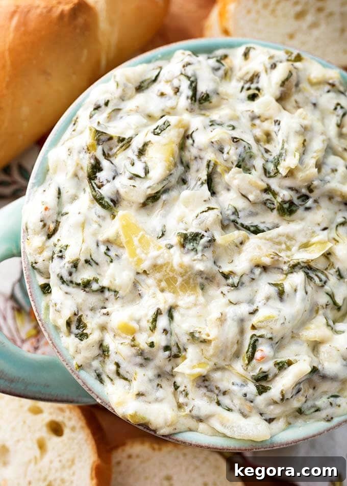 Close up of creamy Instant Pot Spinach Artichoke Dip in a turquoise serving bowl, with crusty bread slices nearby