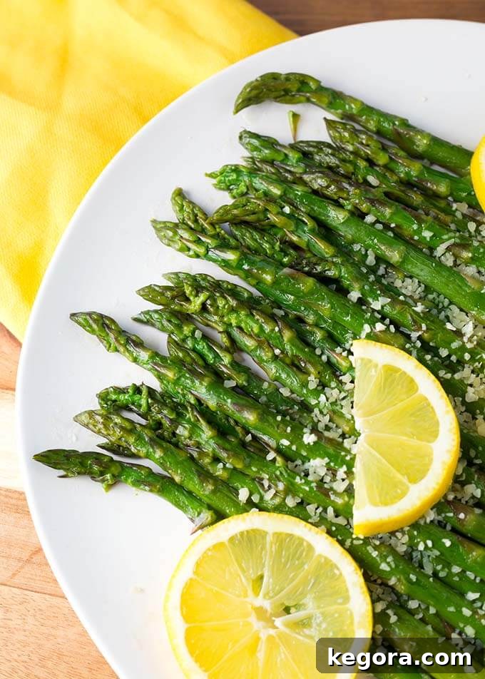 Close-up shot of vibrant green Instant Pot Asparagus spears on a white plate, garnished with a fresh lemon slice, highlighting the appealing texture and bright color of the vegetable.
