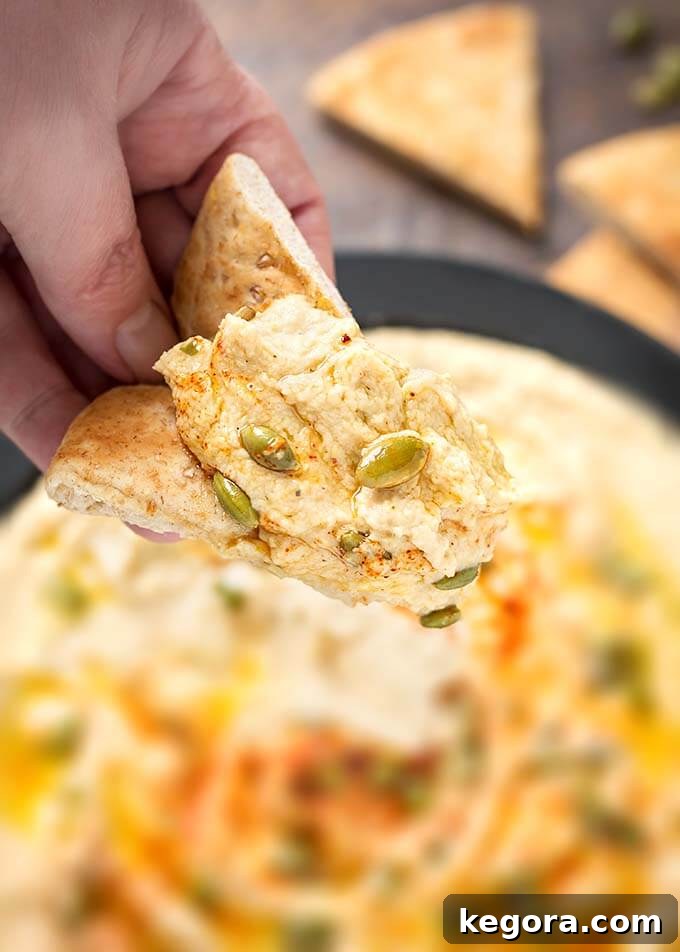 Hand holding a piece of flatbread dipped in Hummus, showcasing its creamy texture