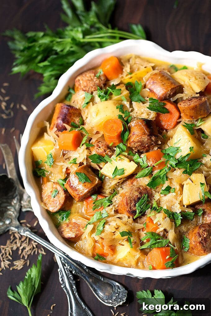 Quick Instant Pot Kielbasa and Sauerkraut 3 Instant Pot Kielbasa and Sauerkraut garnished with parsley in a white bowl, accompanied by a silver spoon and fork