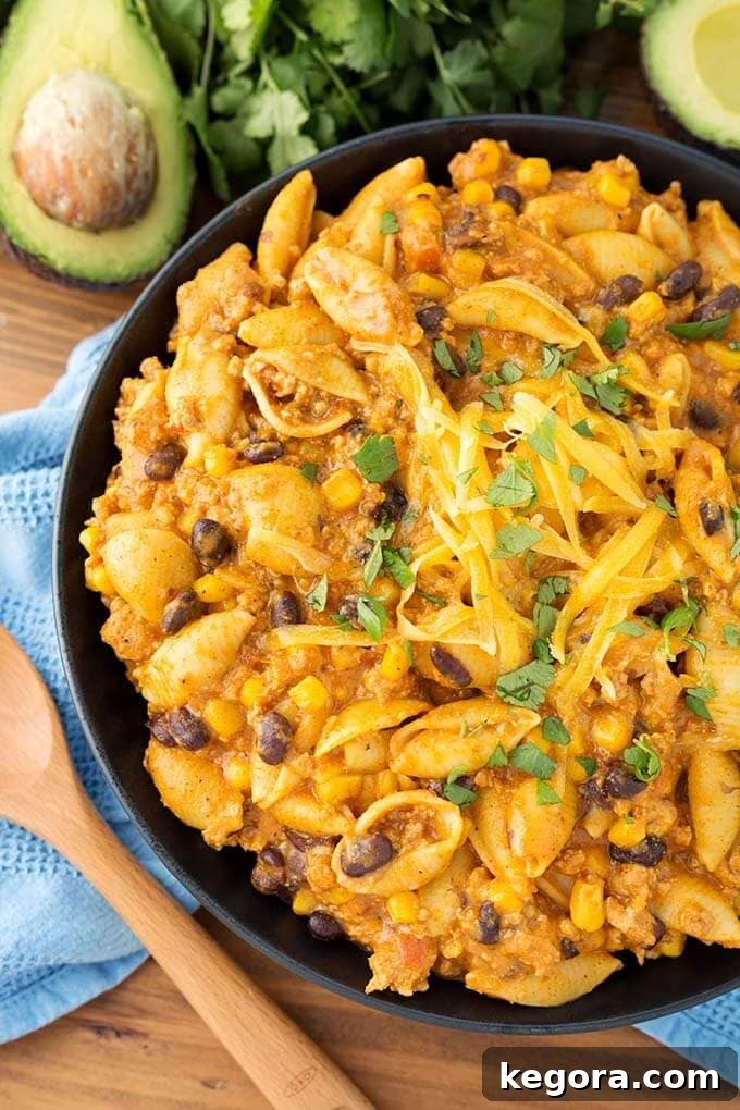 Instant Pot Taco Fiesta Pasta 3 Close-up of Instant Pot Loaded Taco Pasta on a black plate, next to a wooden spoon and fresh avocado slices