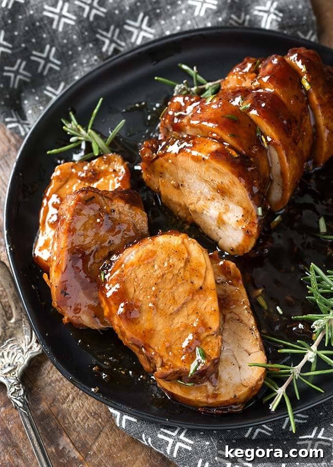 Sliced Honey Garlic Pork Tenderloin with rosemary garnish on black plate, ready to serve