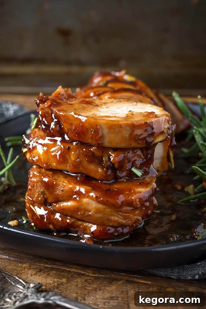 Stacked sliced Honey Garlic Pork Tenderloin on black plate, highlighting the perfectly cooked interior