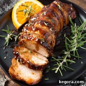 Sliced Honey Garlic Pork Tenderloin garnished with fresh rosemary on black plate, visually appealing