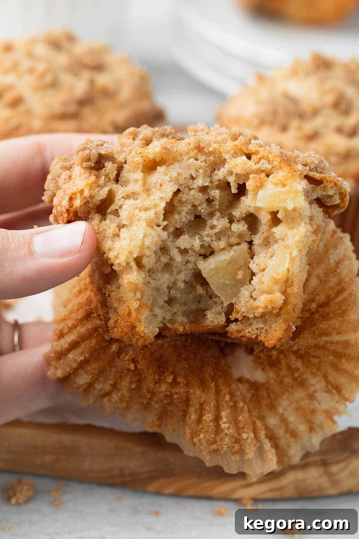 A perfectly baked gluten-free apple muffin with a bite taken out, revealing its soft, apple-filled interior and a golden crumb topping.