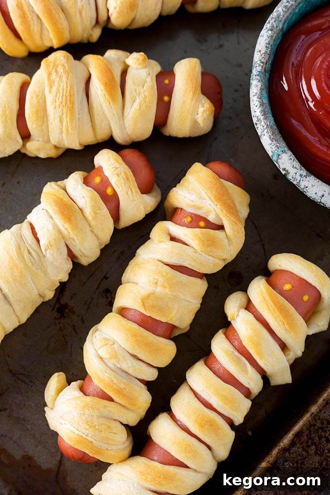 Baked Halloween Hot Dog Mummies on baking sheet with small bowl of ketchup