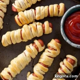 Halloween Hot Dog Mummies on baking sheet with small bowl of ketchup