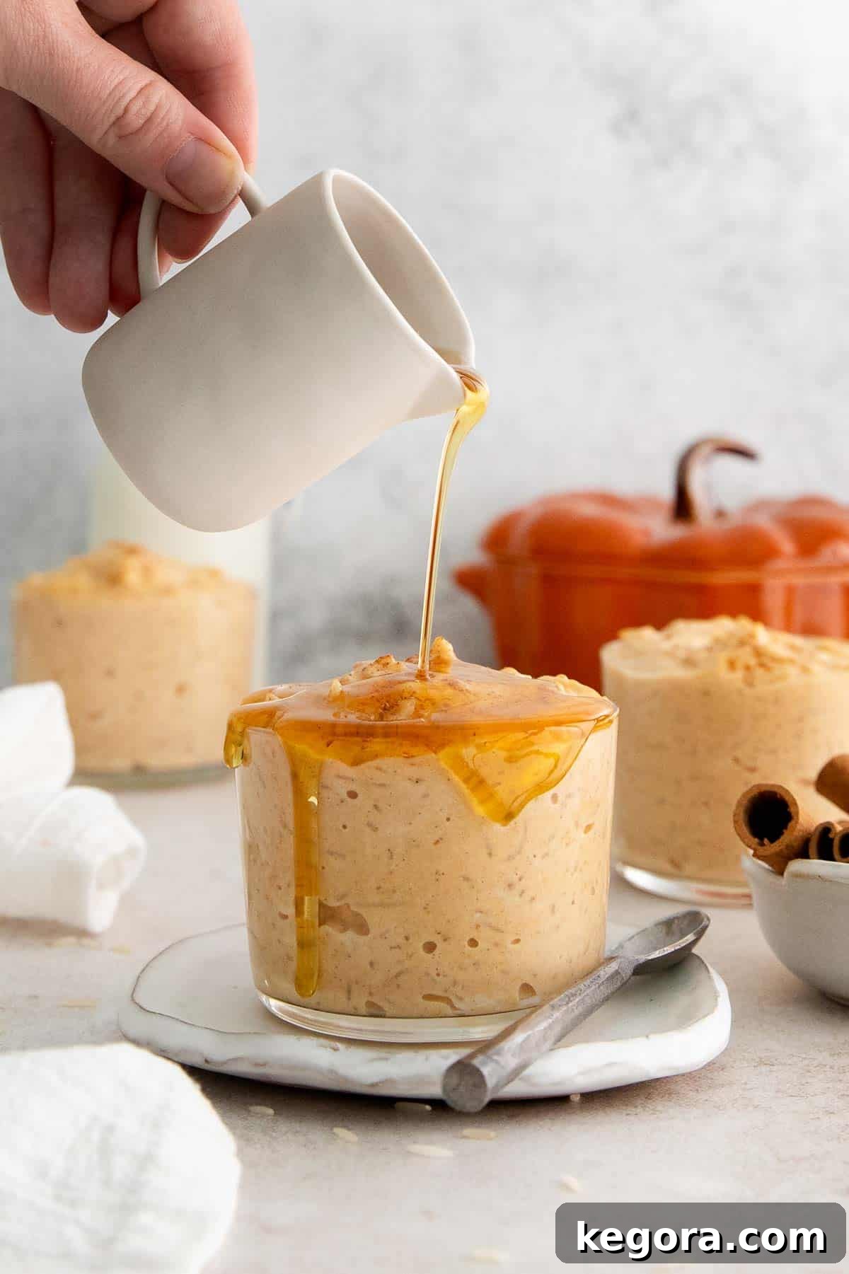 Spiced Pumpkin Rice Pudding 3 A glass bowl of creamy pumpkin rice pudding with rich maple syrup being drizzled on top, ready to serve.