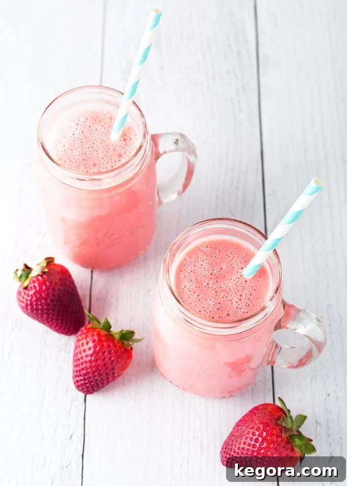 Two Strawberry Sunshine Smoothies in glass mugs with striped straws on a light wood background, surrounded by fresh strawberries.