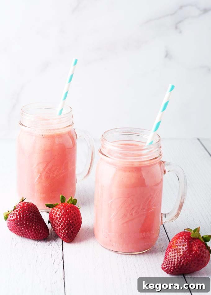 Two Strawberry Sunshine Smoothies with striped straws in glass mugs, accompanied by fresh strawberries.