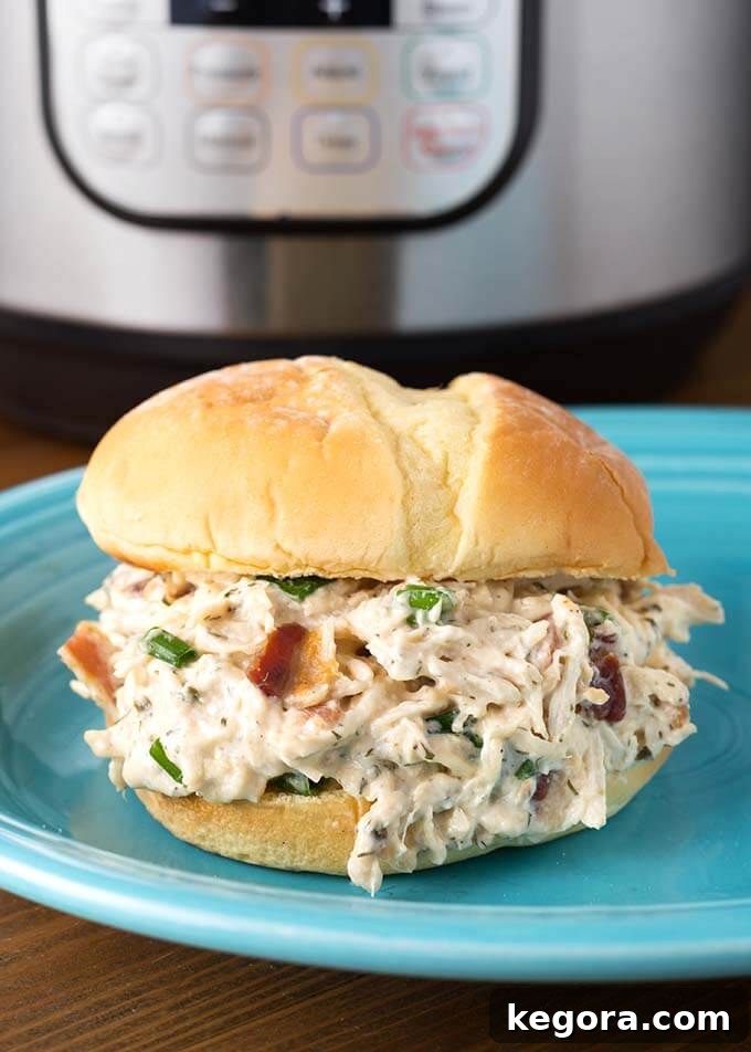 Instant Pot Creamy Dream Chicken 2 Crack Chicken on a hamburger bun on a blue plate in front of pressure cooker