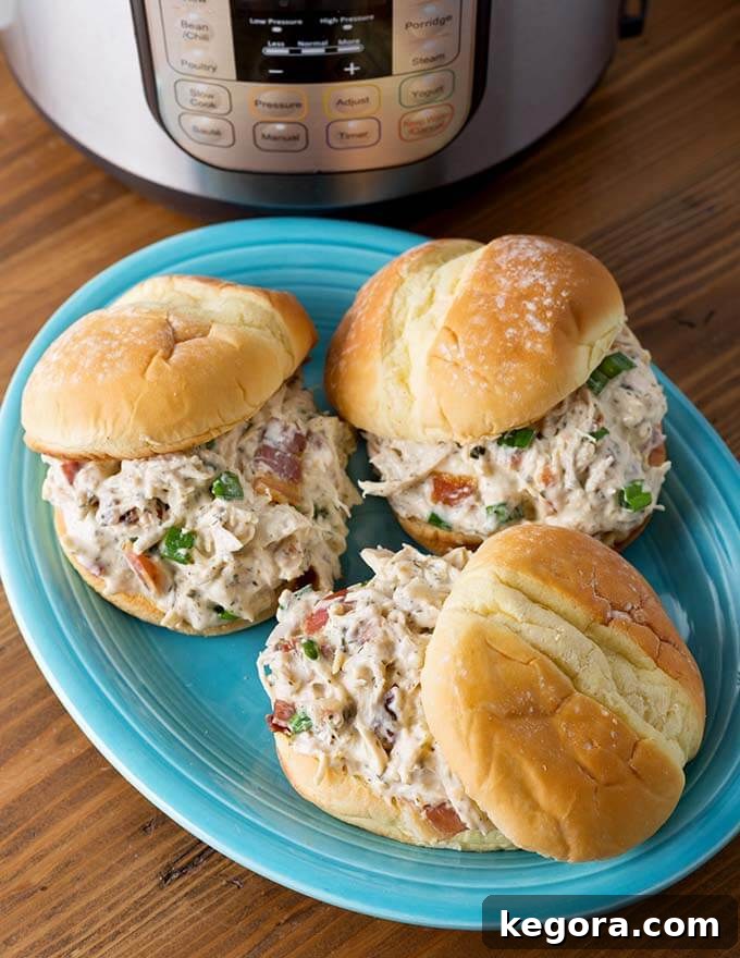 Instant Pot Creamy Dream Chicken 4 Three hamburger buns with Crack Chicken on blue plate in front of a pressure cooker