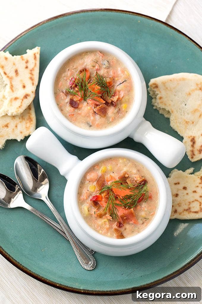 Artisan Salmon Chowder 15 Two white bowls of Salmon Chowder on a turquoise plate with two silver spoons and torn flat bread, ready to be served.