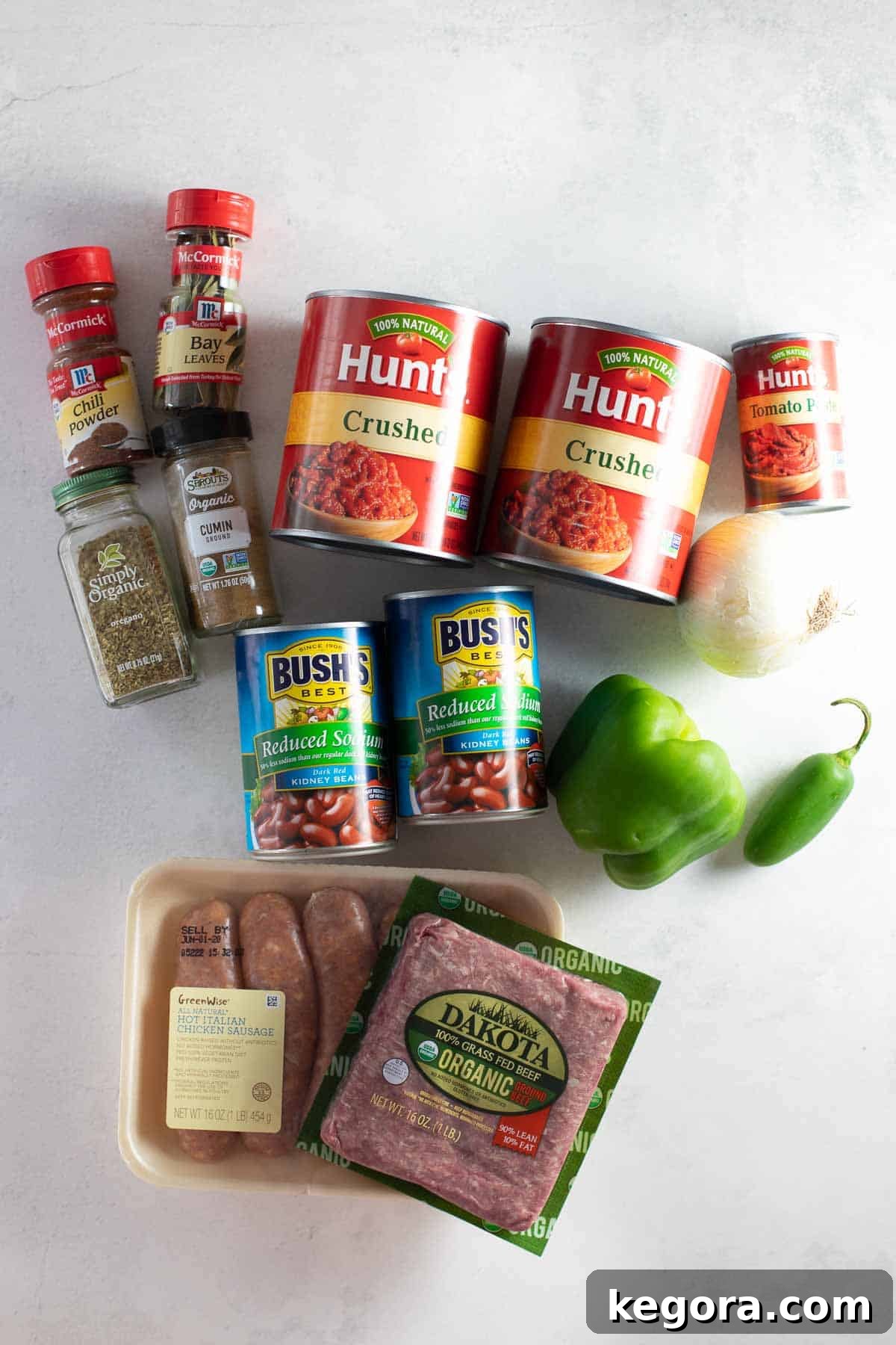 Hearty Gluten-Free Chili 3 A vibrant selection of fresh ingredients laid out on a marble background, including ground beef, sausage, onions, green peppers, jalapeños, garlic, crushed tomatoes, tomato paste, various spices, brown sugar, chicken stock, and kidney beans, all ready for making delicious gluten-free chili.