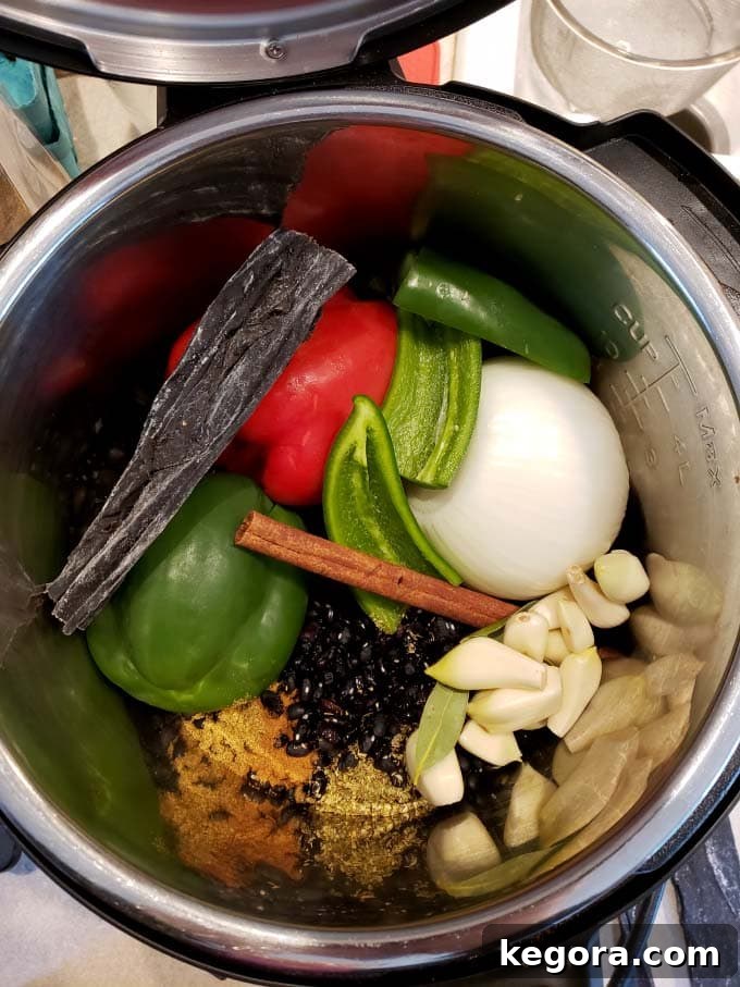 Speedy Cuban Black Beans 3 A collection of whole vegetables including a yellow onion, bell peppers, jalapeños, and garlic cloves, alongside dry black beans, ready to be cooked in an Instant Pot liner.