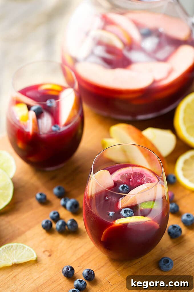 Vibrant Red Fruit Sangria 3 Two Fruity Red Sangria in glasses on a wooden board with a pitcher, blueberries and lemon slices in the background