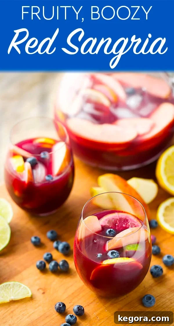 Vibrant Red Fruit Sangria 7 Fruity Red Sangria in a stemless wine glass with a pitcher behind it