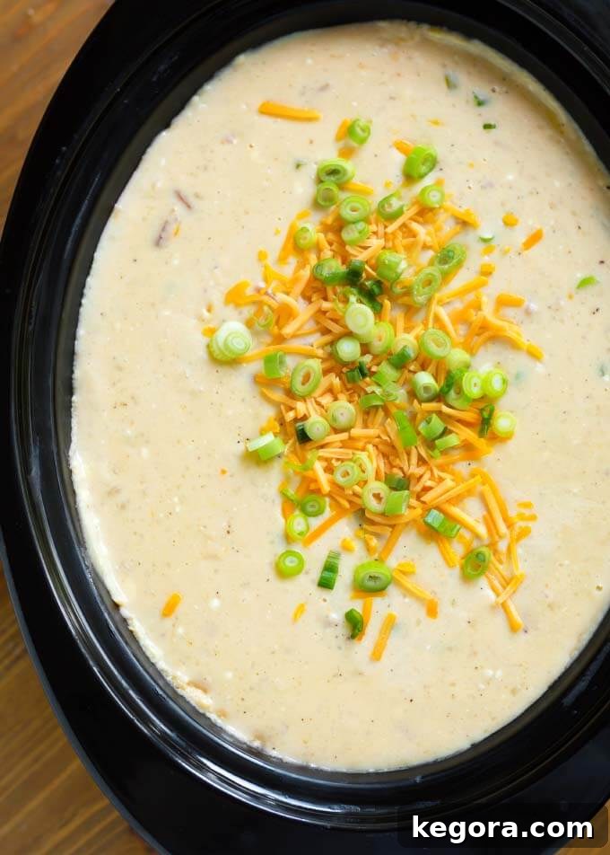 Rich and creamy Loaded Potato Soup simmering in a black slow cooker, adorned with delicious toppings like cheddar cheese and bacon