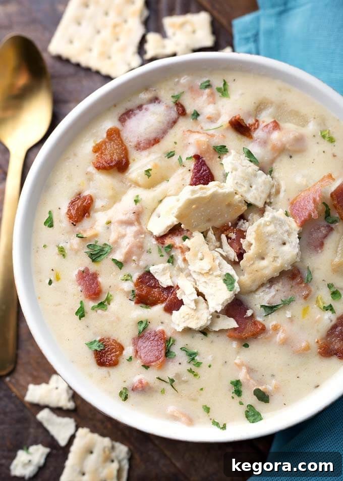 A close-up view of a rich and creamy Slow Cooker Clam Chowder in a white bowl, generously garnished with crumbled oyster crackers, inviting a comforting culinary experience.