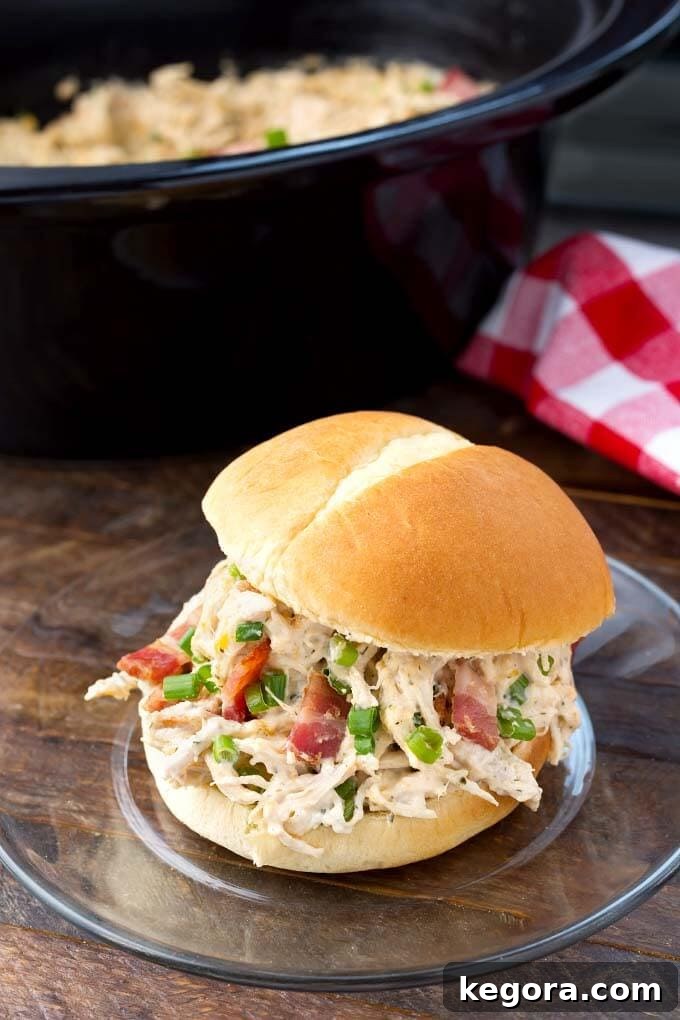 Crack Chicken on a hamburger bun on a glass plate in front of a slow cooker, a perfect serving suggestion