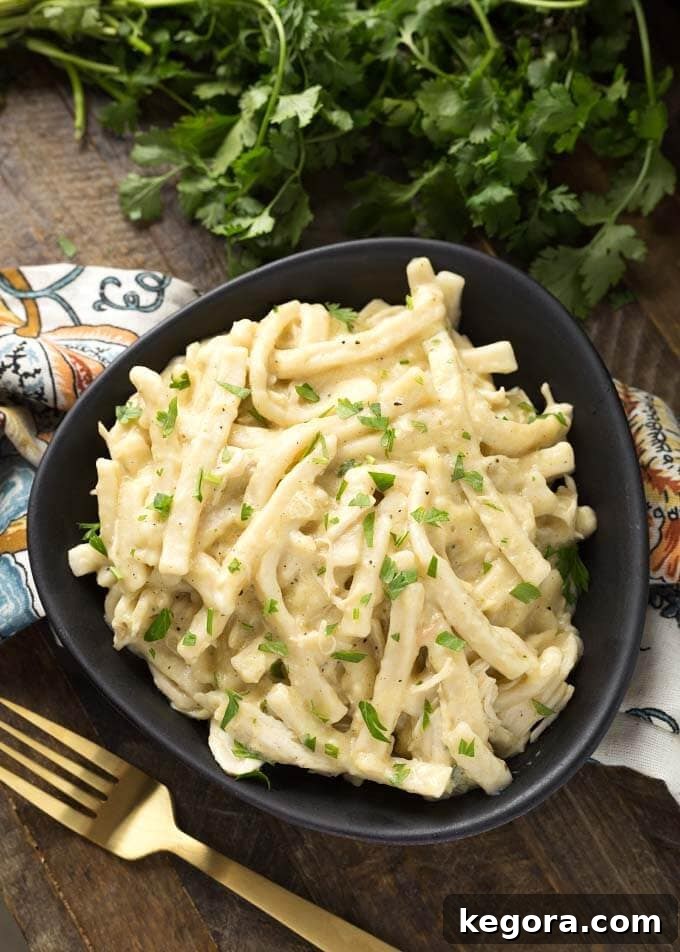 A black bowl filled with creamy Slow Cooker Chicken and Noodles, accompanied by a gold fork on a rustic wooden board.